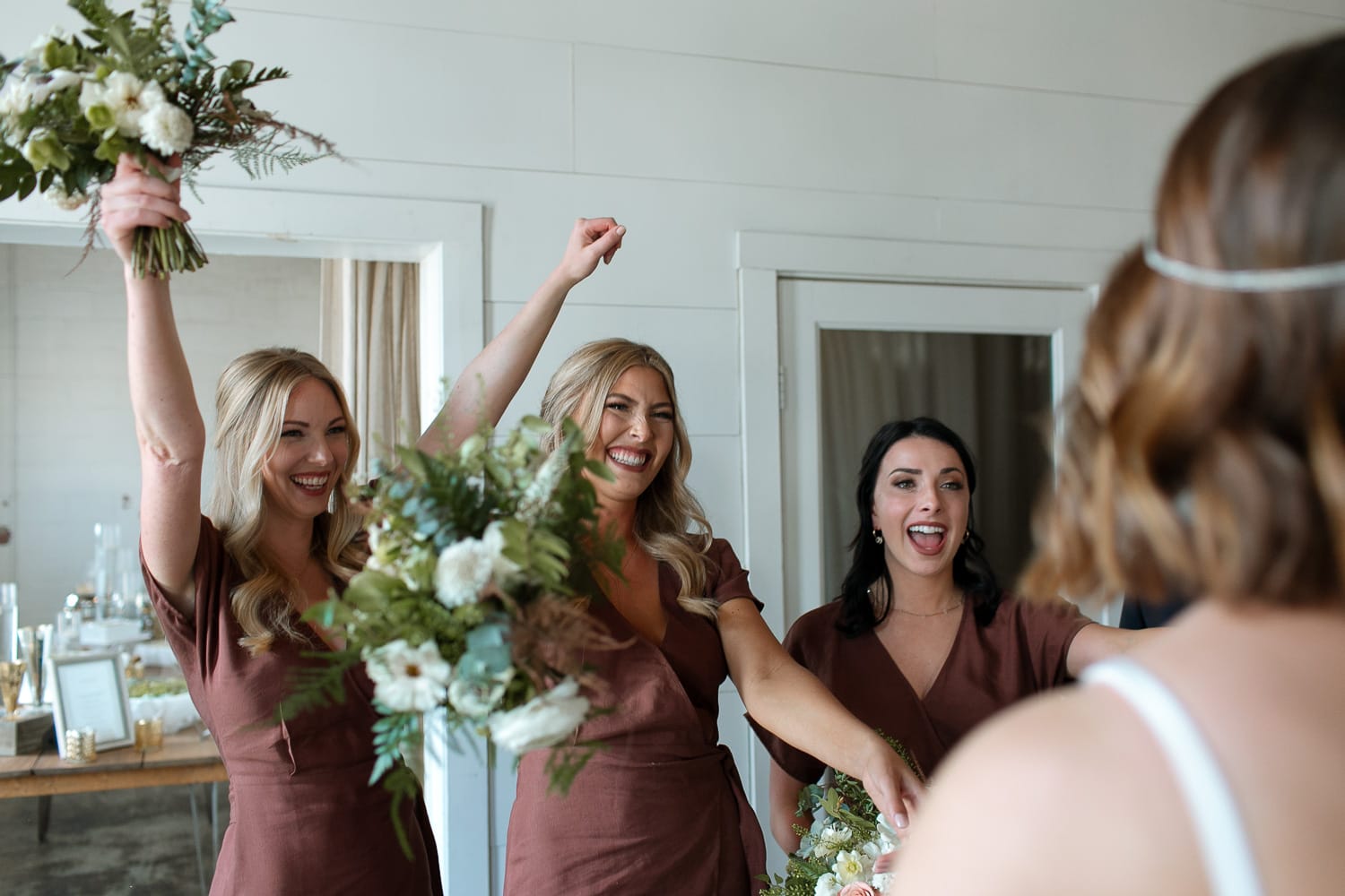 Bridesmaids cheering on the bride. They are holding white and greenery wedding bouquets.