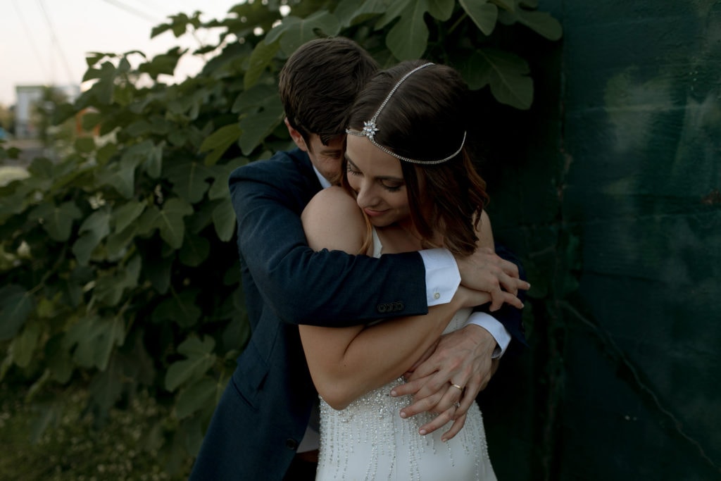 A bride and groom embracing. Their wedding theme is white and greenery.
