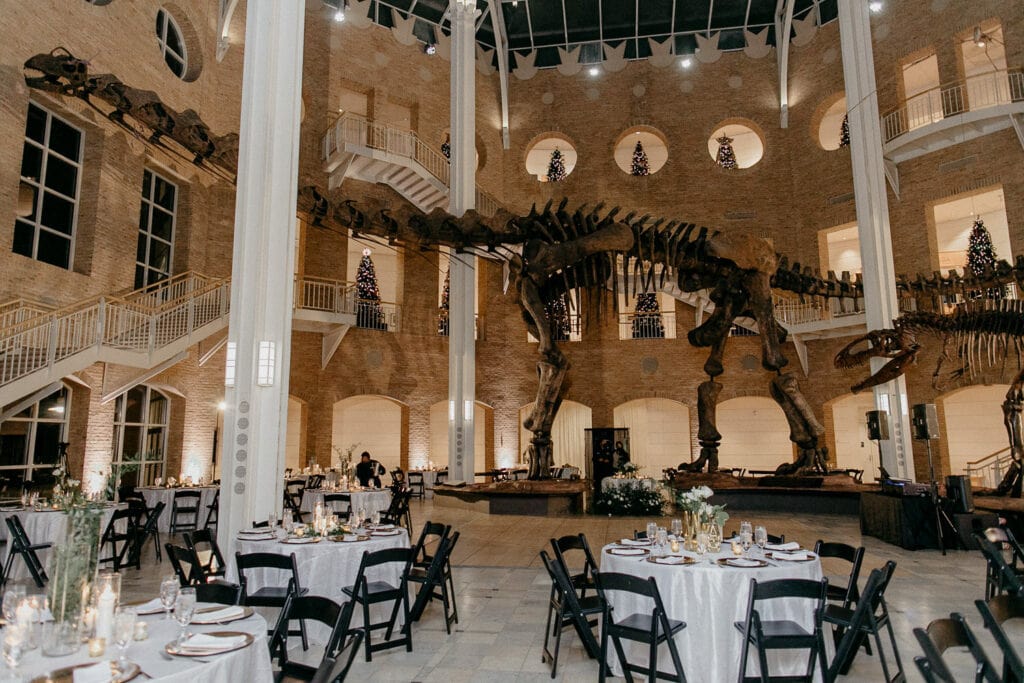A wedding reception tablescape at Fernbank Museum with a large dinosaur fossil overlooking the evening.