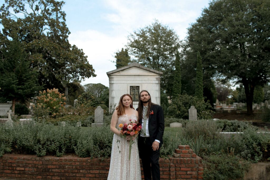 A couple looking at the camera in their wedding clothes at Oakland Cemetery. 